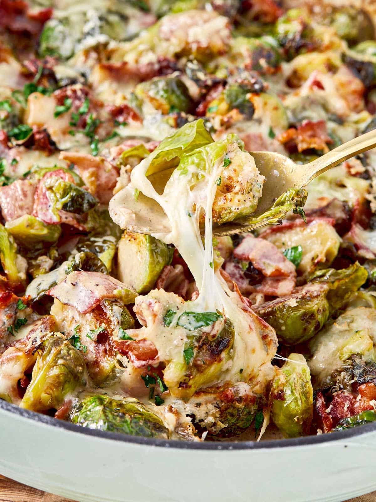Close-up of cheesy Brussels sprouts and bacon with gooey mozzarella stretching from the pan