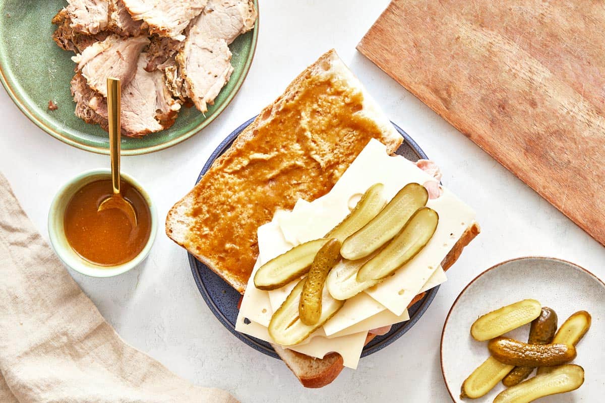 Cuban sandwich being assembled with pork, cheese, and pickles.