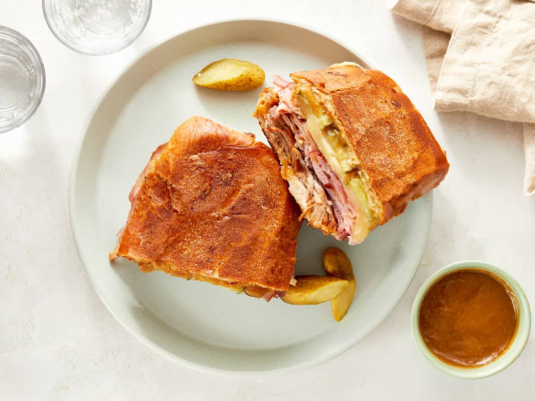 Cuban sandwich cut in half on a plate with pickles.