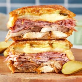 Stacked Cuban sandwich with layers of roast pork, ham, salami, Swiss cheese, pickles, and mustard, pressed until golden and melty.