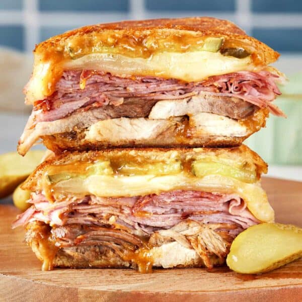 Stacked Cuban sandwich with layers of roast pork, ham, salami, Swiss cheese, pickles, and mustard, pressed until golden and melty.