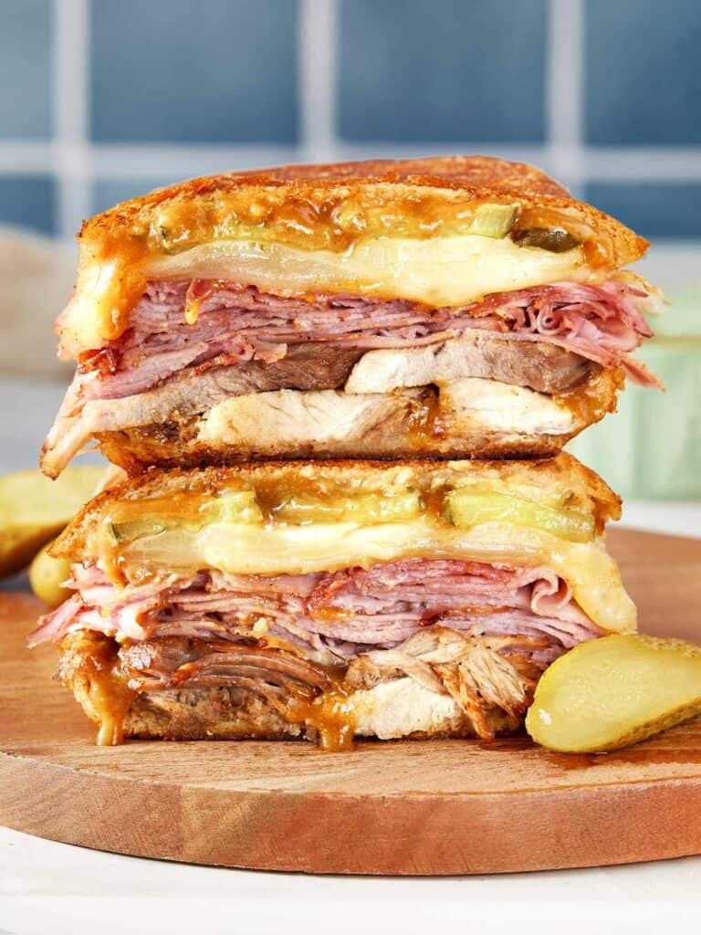 Stacked Cuban sandwich with layers of roast pork, ham, salami, Swiss cheese, pickles, and mustard, pressed until golden and melty.