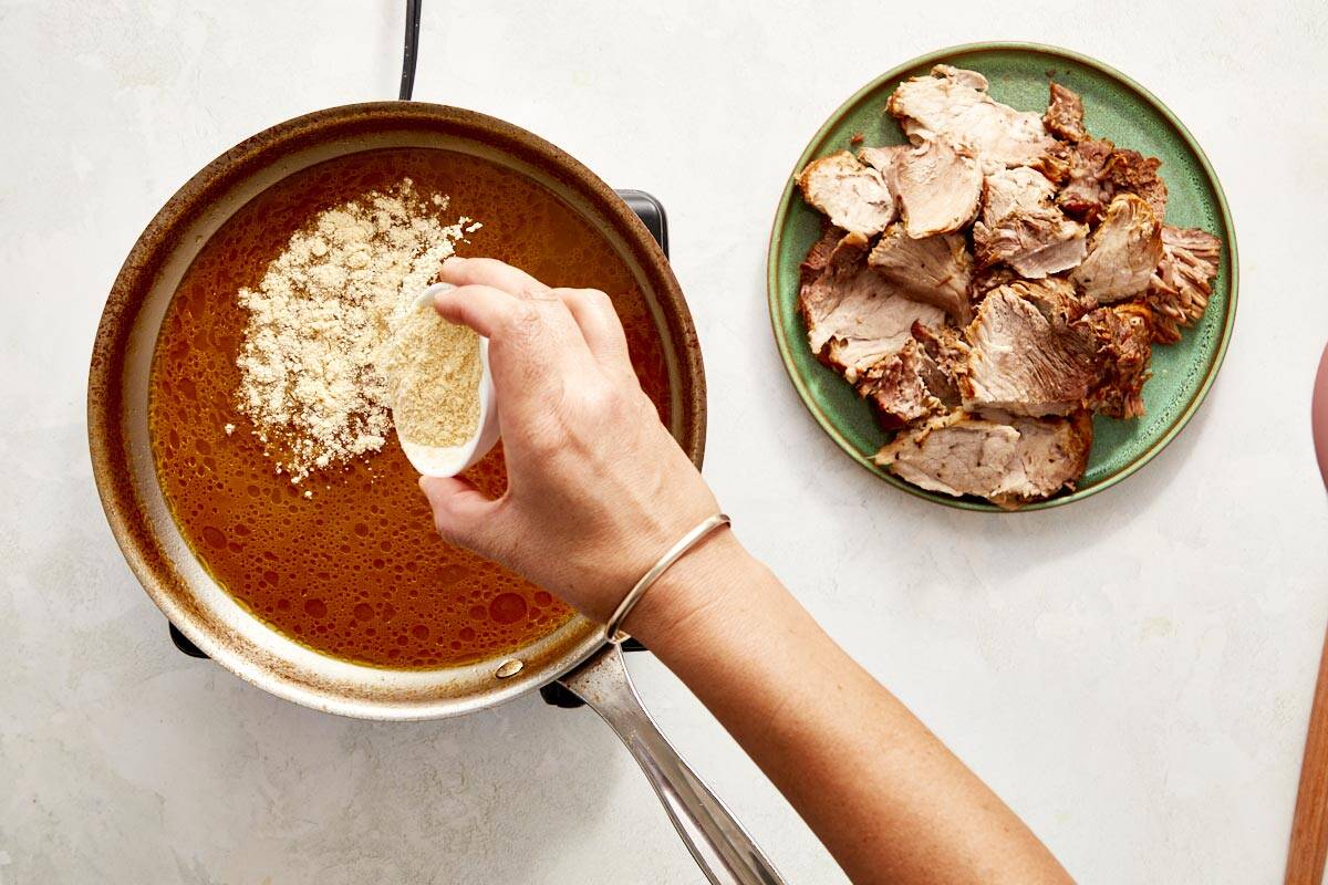 Hand adding cornflour to sauce in a pan