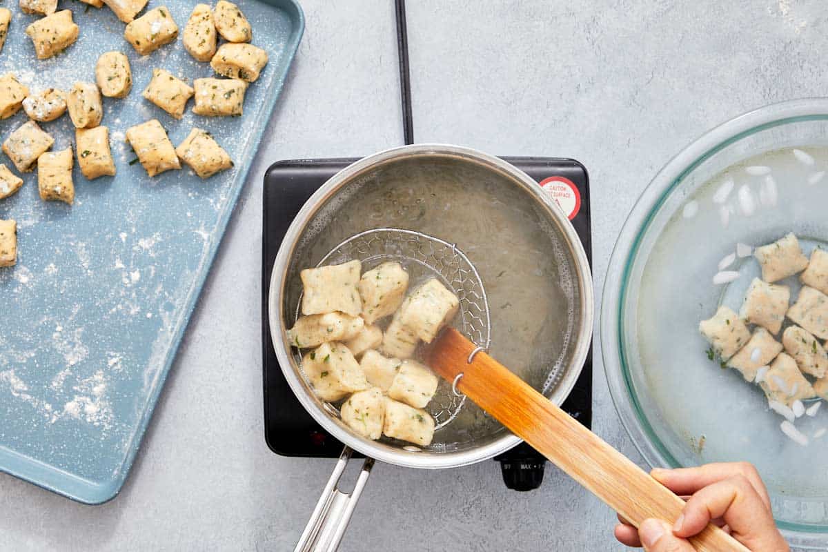 Gnocchi pieces boiling in water with a strainer spoon.