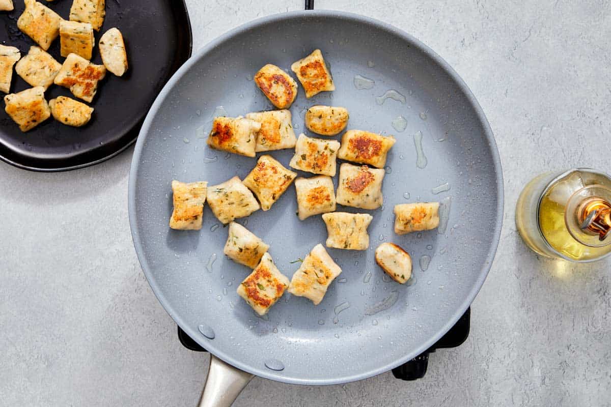Golden brown gnocchi frying in a pan with olive oil.