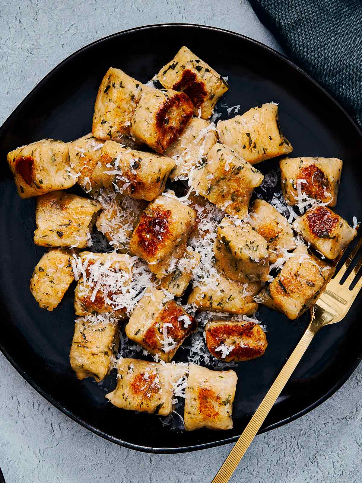 Golden brown gnocchi topped with grated parmesan on a black plate.