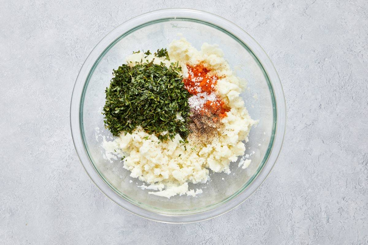 Mashed potatoes with chopped herbs and spices in a bowl.