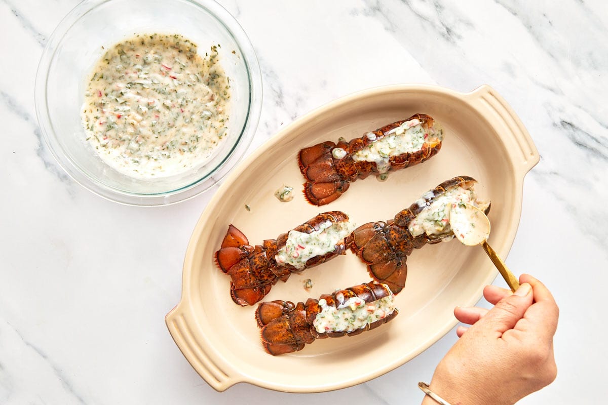 Chimichurri butter being spooned over raw lobster tails before broiling.