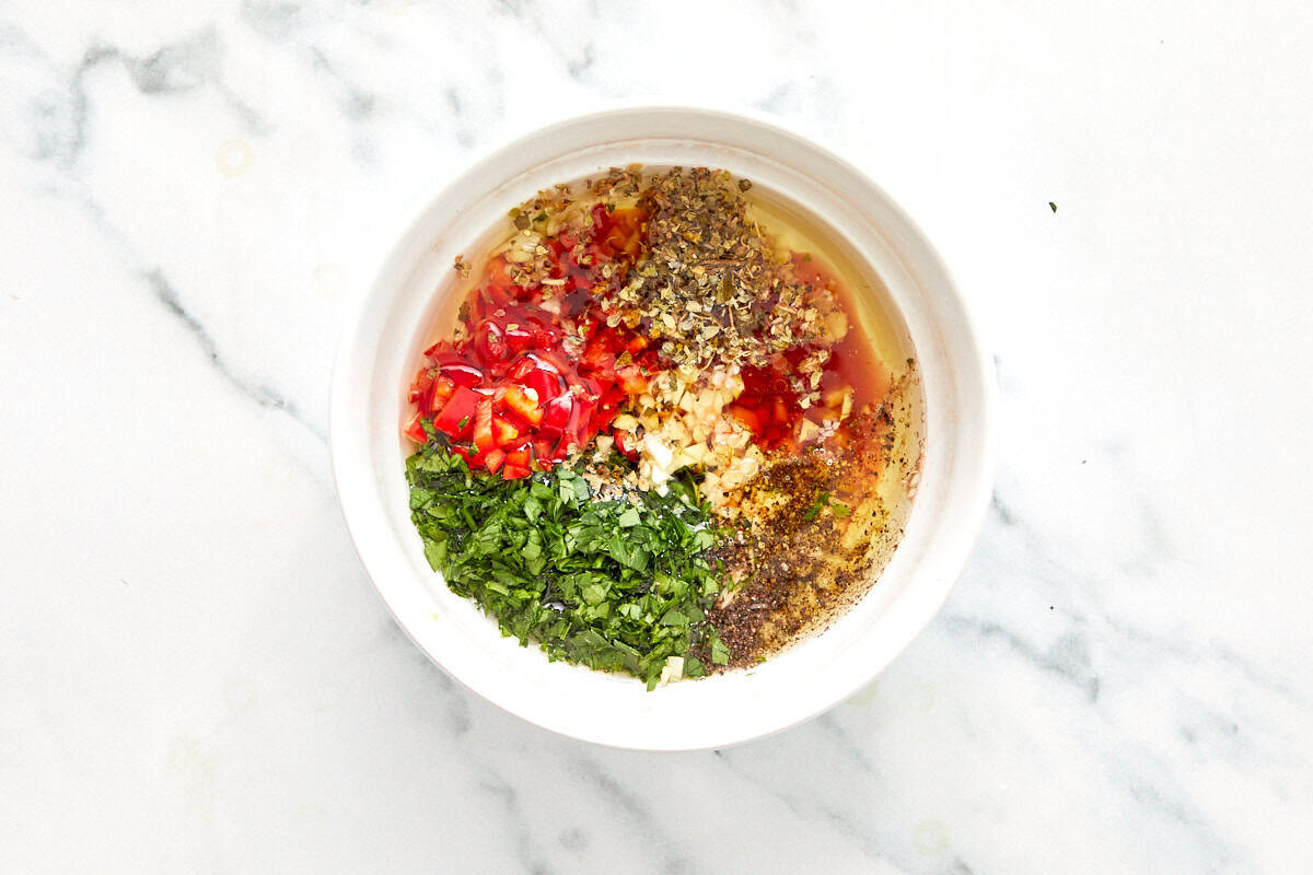Bowl with chopped parsley, garlic, red chili, oregano, and black pepper ready to be mixed with olive oil and vinegar for chimichurri.