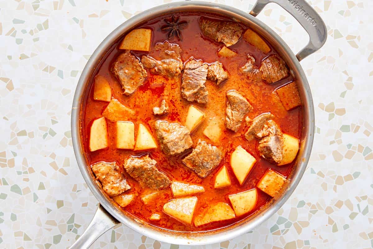 Beef and potatoes simmering in red curry sauce.