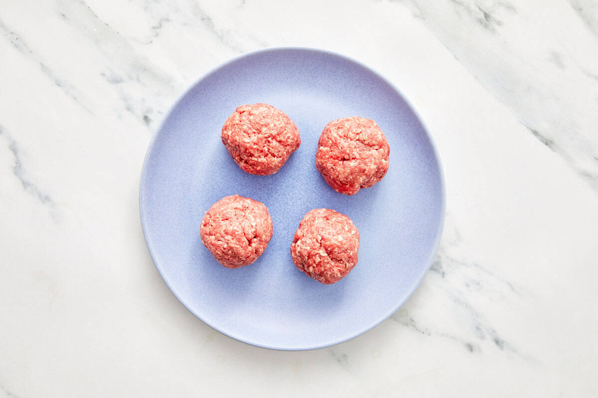 Four raw ground beef balls on a light blue plate.