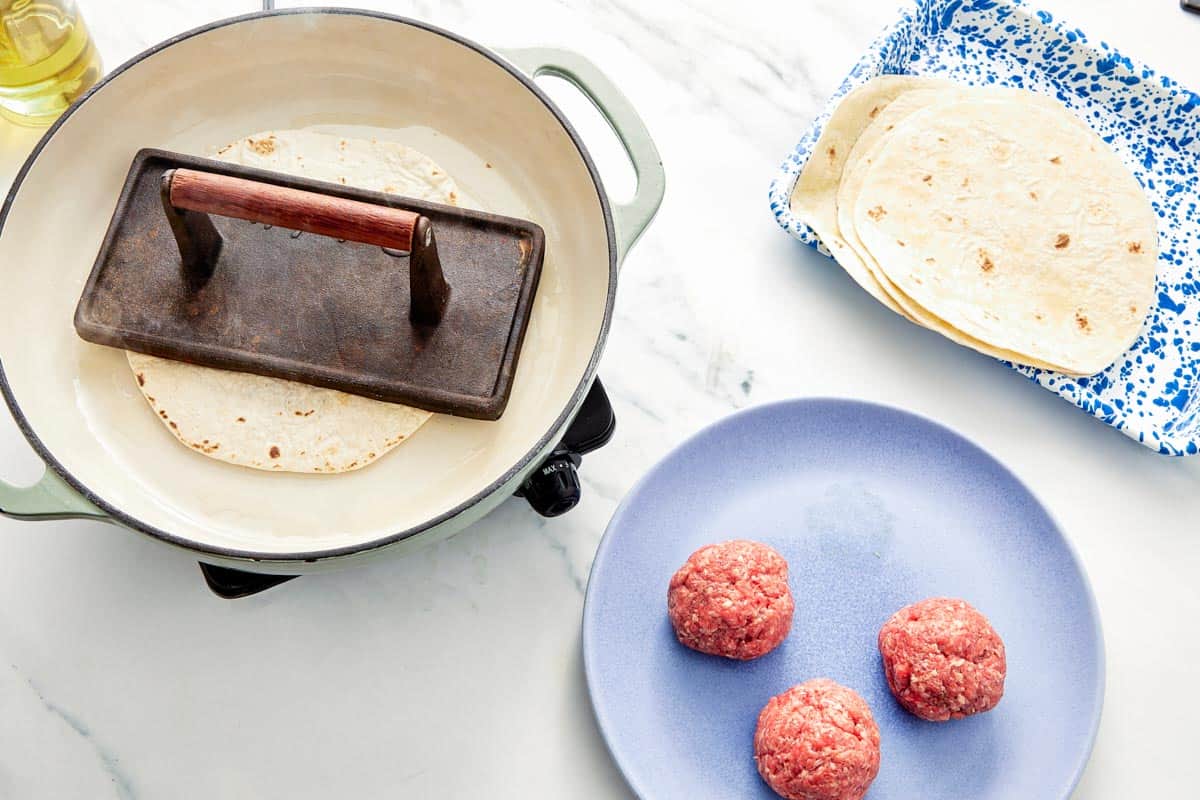 Tortilla with beef being pressed down in a skillet using a metal grill press