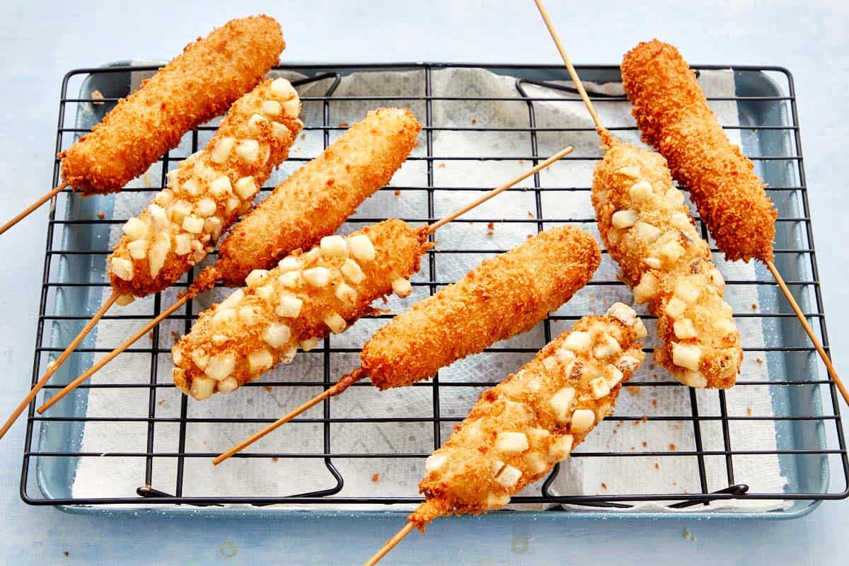 Golden, crispy Korean corn dogs cooling on a wire rack with diced fries coating.