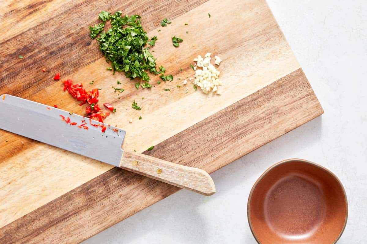 Chopped chilli, cilantro, and minced garlic on a board with a knife.