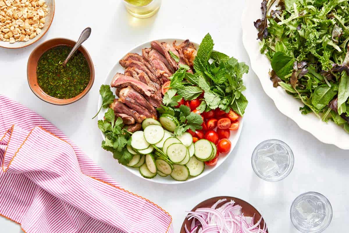 Salad components arranged—steak, cucumber, tomatoes, herbs, dressing.