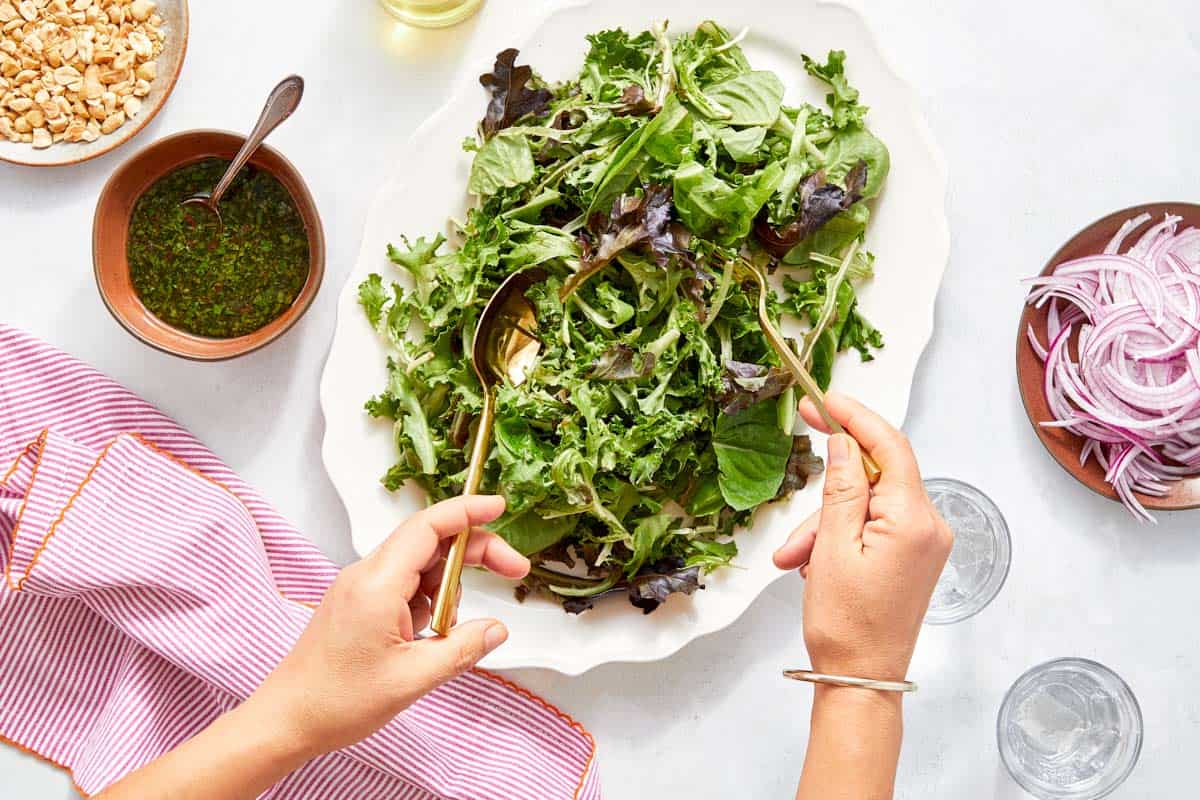 Tossing mixed greens with dressing in a large platter.