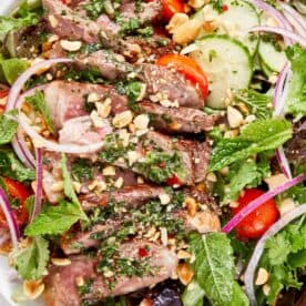 Thai beef salad with sliced seared steak, mixed greens, cucumber, cherry tomatoes, red onion, fresh herbs, and chopped peanuts. - 15