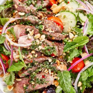 Thai beef salad with sliced seared steak, mixed greens, cucumber, cherry tomatoes, red onion, fresh herbs, and chopped peanuts.