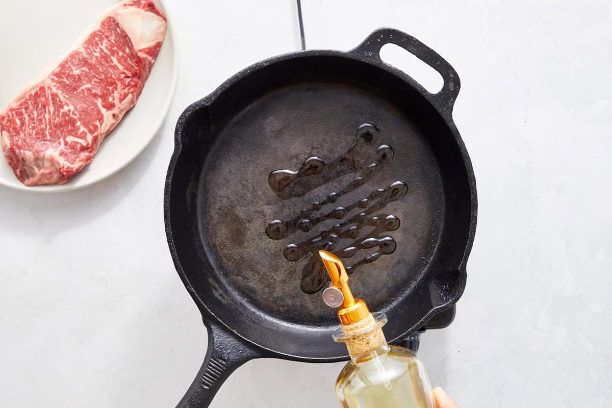 Oiled cast-iron skillet ready for searing; steak beside the pan.