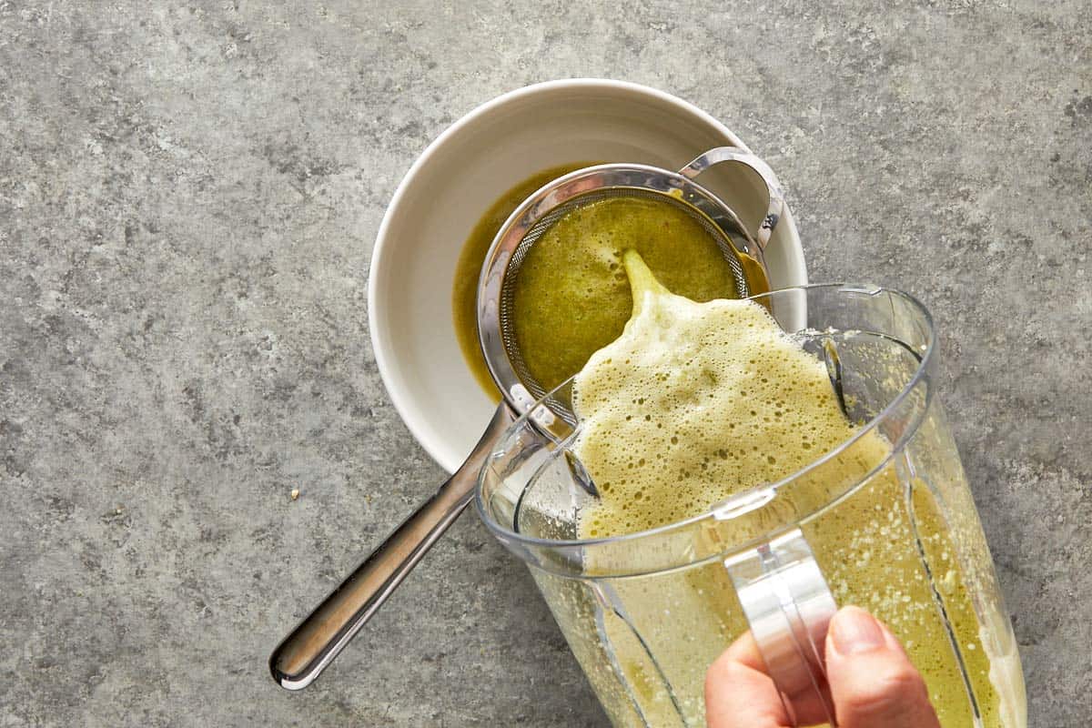 Straining the blended marinade through a fine mesh sieve into a bowl.