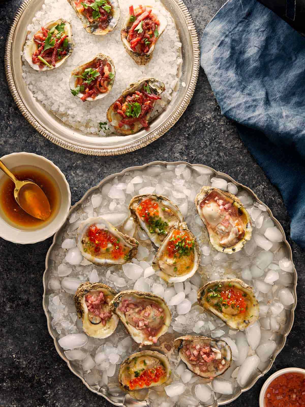Plates of oysters served three ways, with toppings like red onion, herbs, and roe on ice and salt.