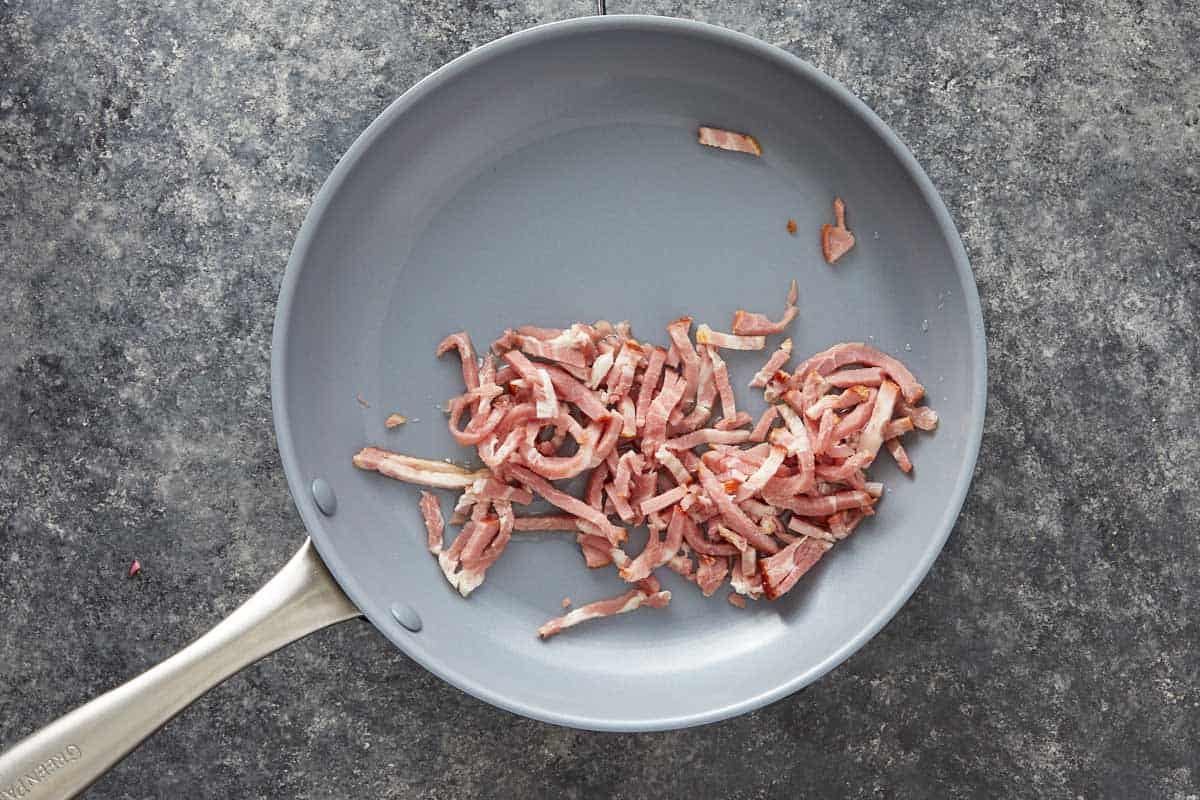 Crispy bacon strips cooking in a gray skillet.
