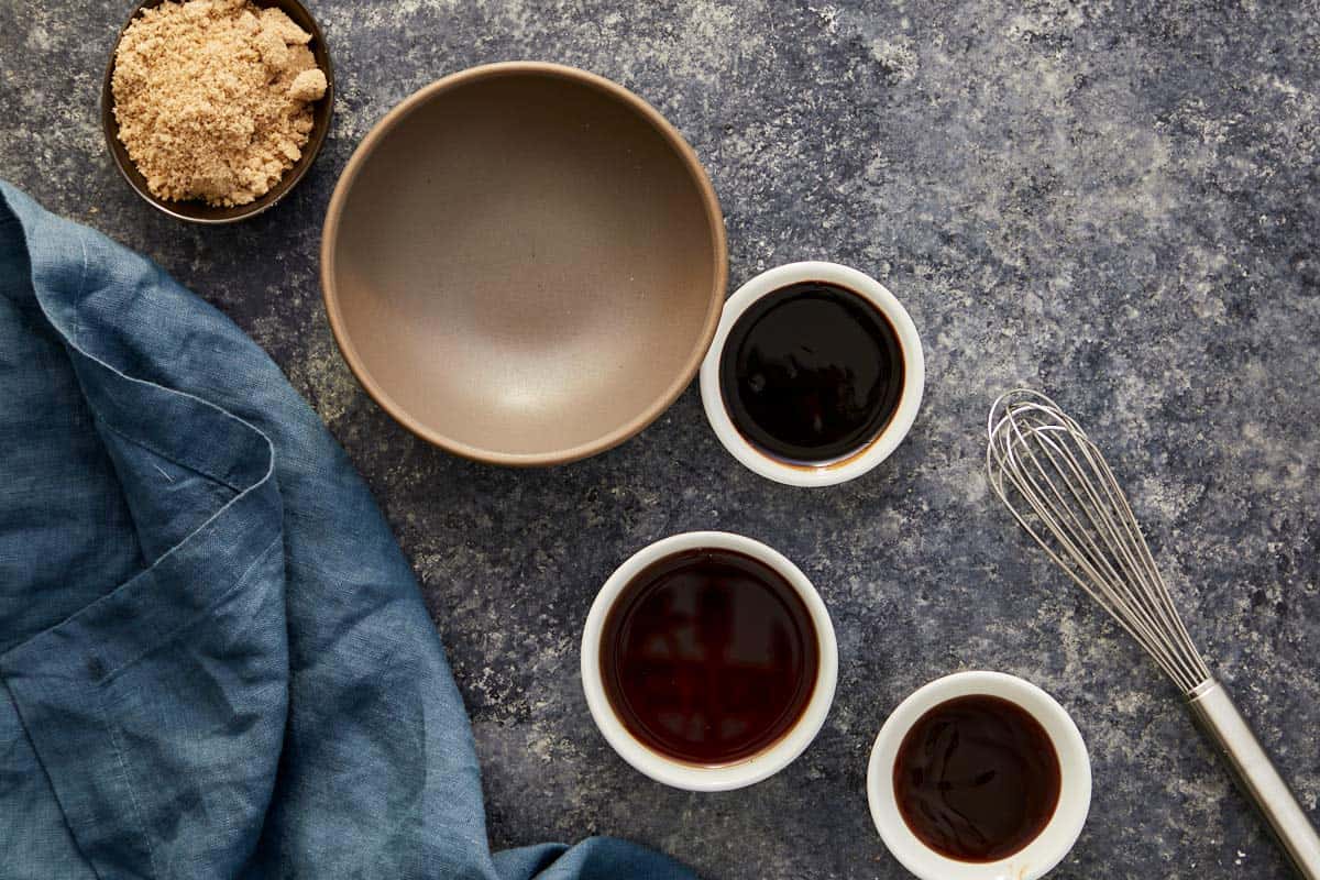 Small bowls with tamarind purée, fish sauce, oyster sauce, and brown sugar next to a whisk