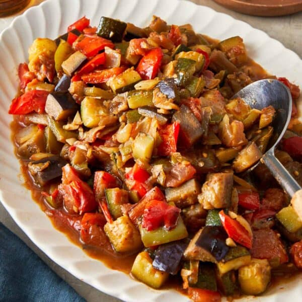 A vibrant plate of Ratatouille vegetables, with a spoon and a glass of wine elegantly placed nearby.