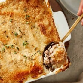 Spoonful of Shepherd’s Pie being served from a white baking dish, showing beef filling and mashed potato topping.
