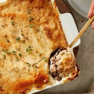 Spoonful of Shepherd’s Pie being served from a white baking dish, showing beef filling and mashed potato topping.