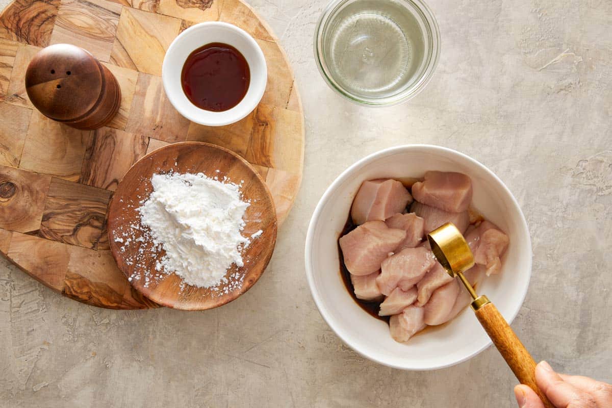 Raw chicken chunks in a bowl with soy sauce, cornstarch, and water.