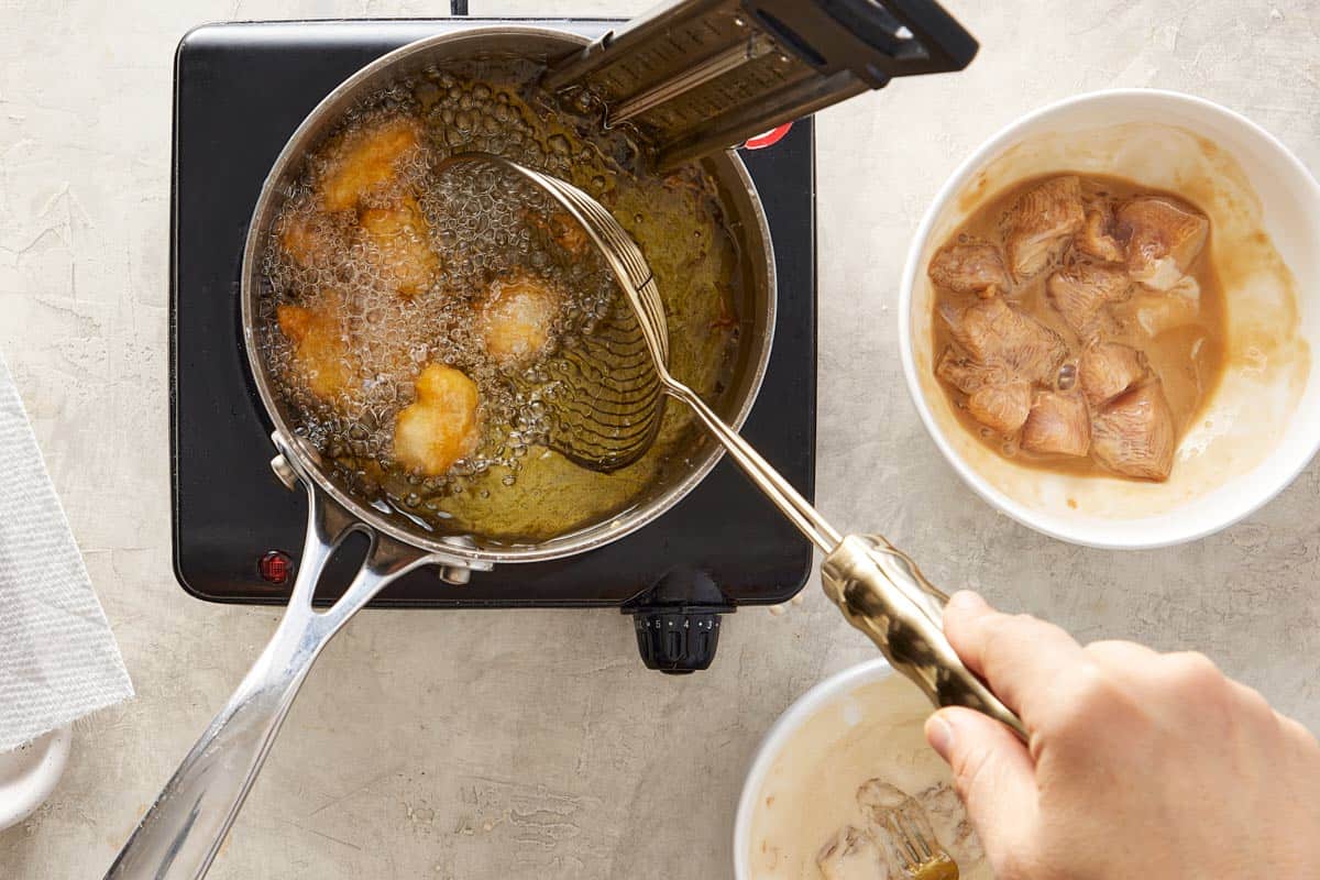 Chicken pieces frying in hot oil in a pot.
