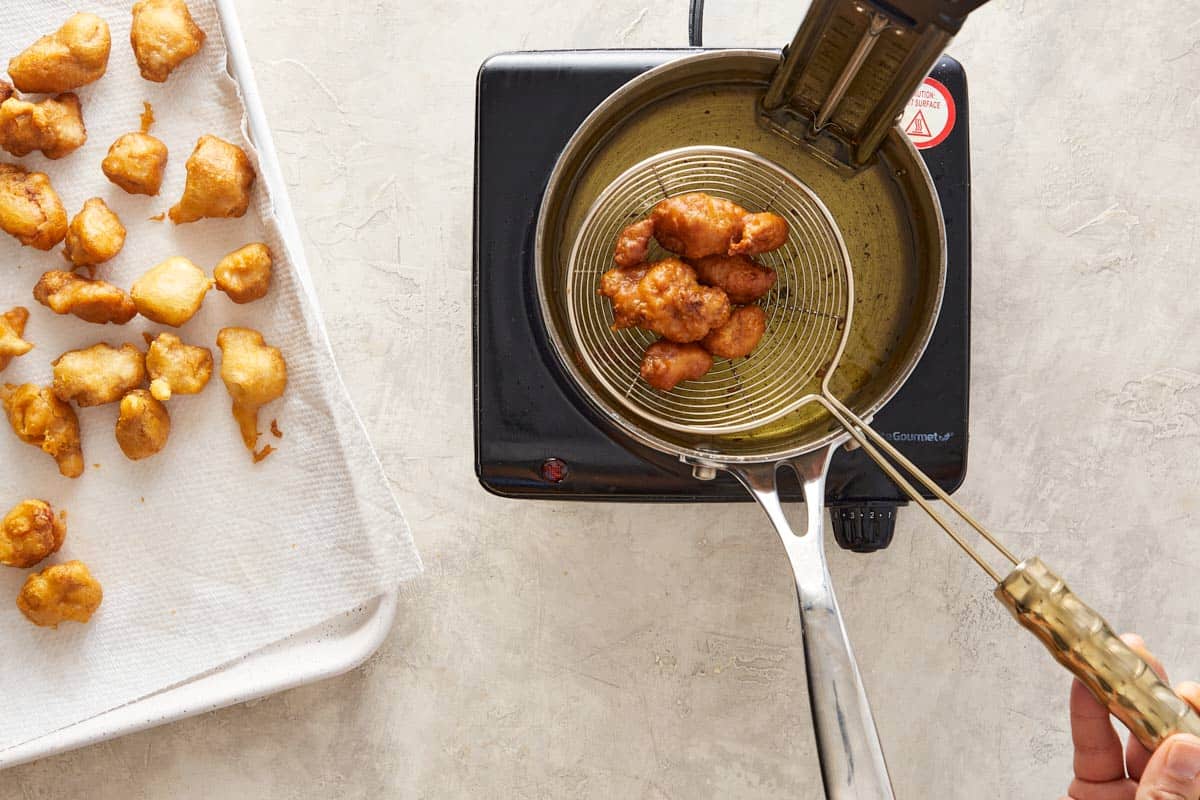 Fried chicken pieces being removed from hot oil to a tray.