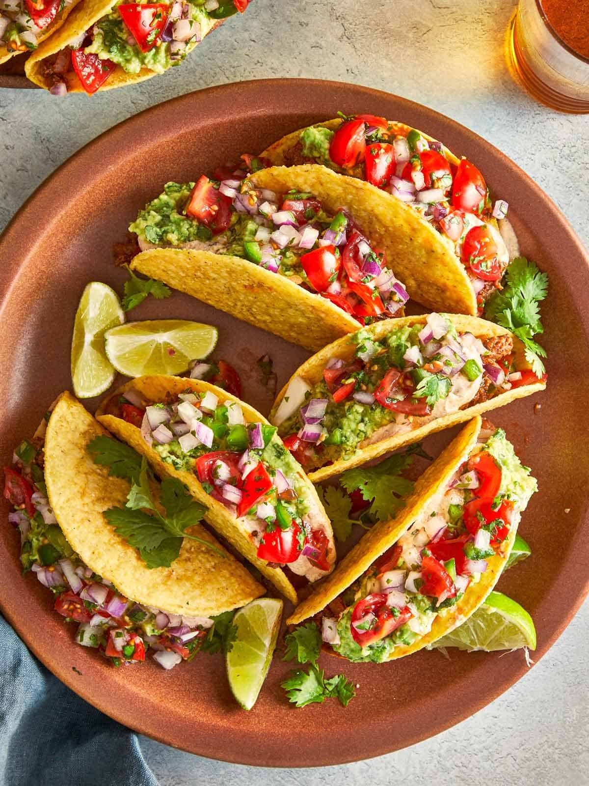 Plate of beef tacos with guacamole, salsa, and lime wedges