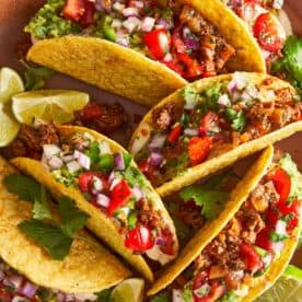 Beef tacos with guacamole, salsa, and lime wedges on a plate