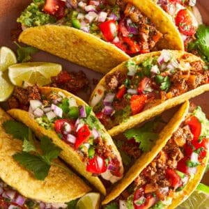 Beef tacos with guacamole, salsa, and lime wedges on a plate