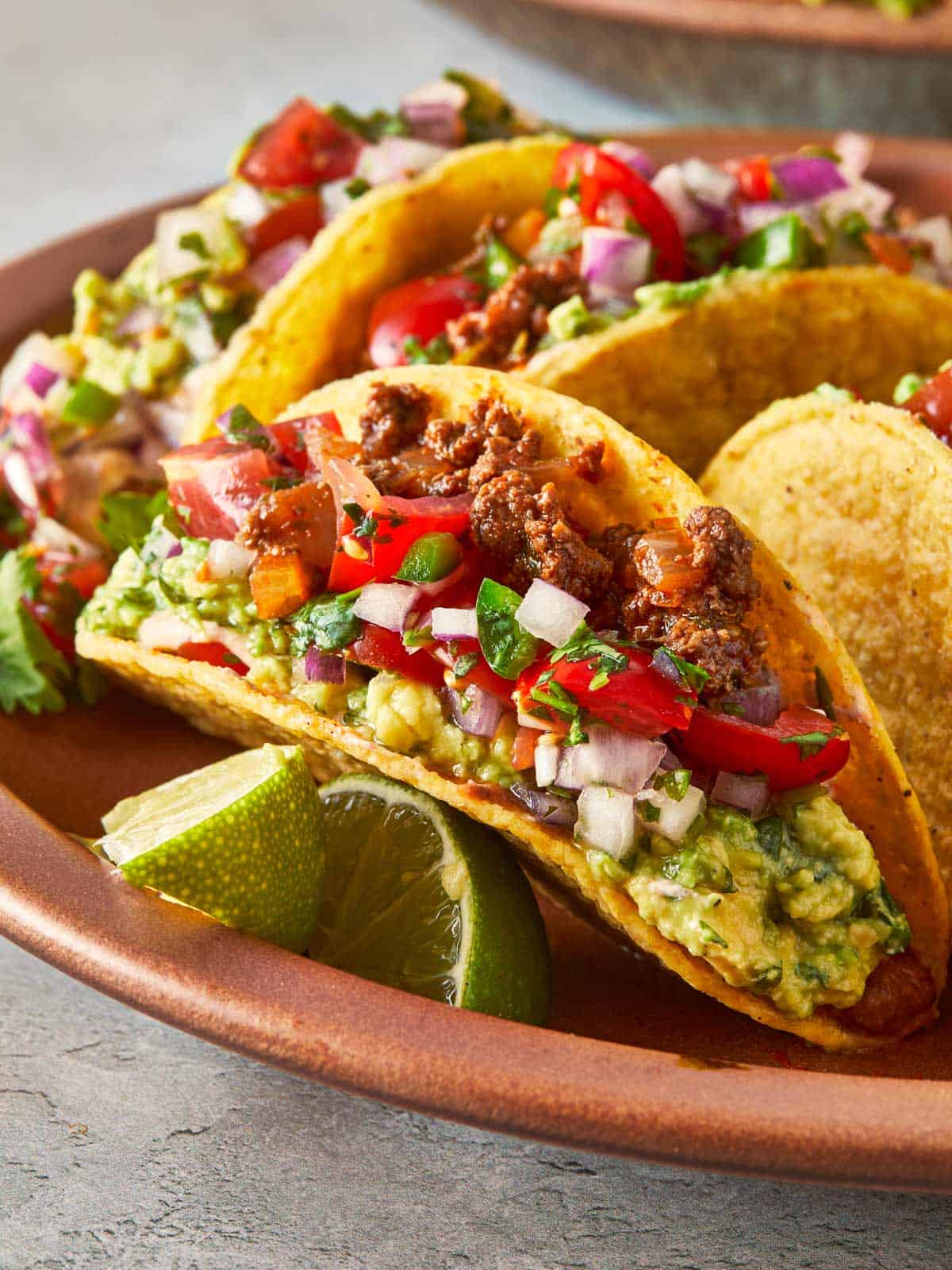 Close-up of a beef taco with guacamole, salsa, and lime wedges on a plate