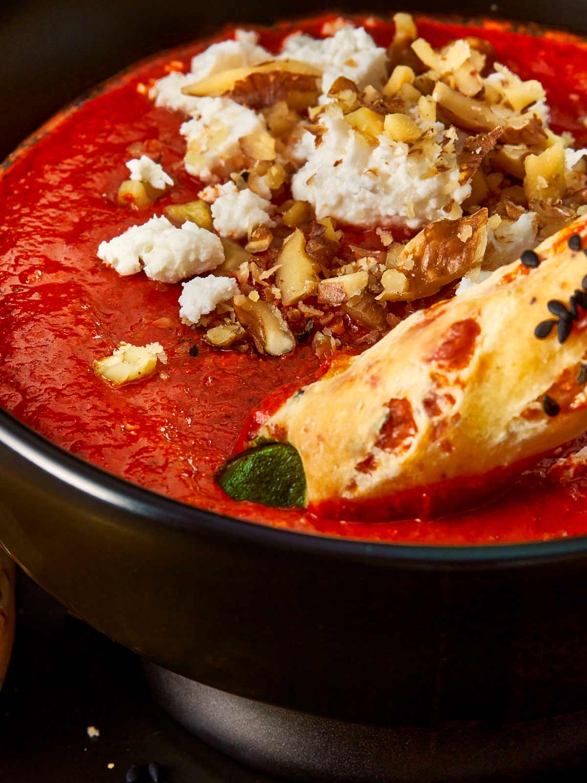 Close-up of a Halloween-themed Bloody Dip — a deep red roasted pepper and tomato spread topped with crumbled feta and chopped walnuts, served with a witch finger grissini dipped into the sauce.