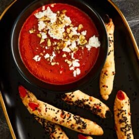 Halloween-themed Bloody Dip — a deep red roasted pepper and tomato spread topped with crumbled feta and chopped walnuts, served with witch fingers grissini
