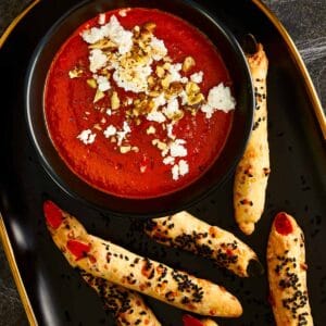 Halloween-themed Bloody Dip — a deep red roasted pepper and tomato spread topped with crumbled feta and chopped walnuts, served with witch fingers grissini