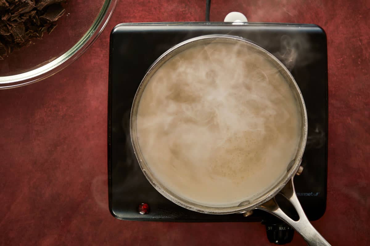 Heating cream on the stove until steaming to prepare the chocolate ganache.