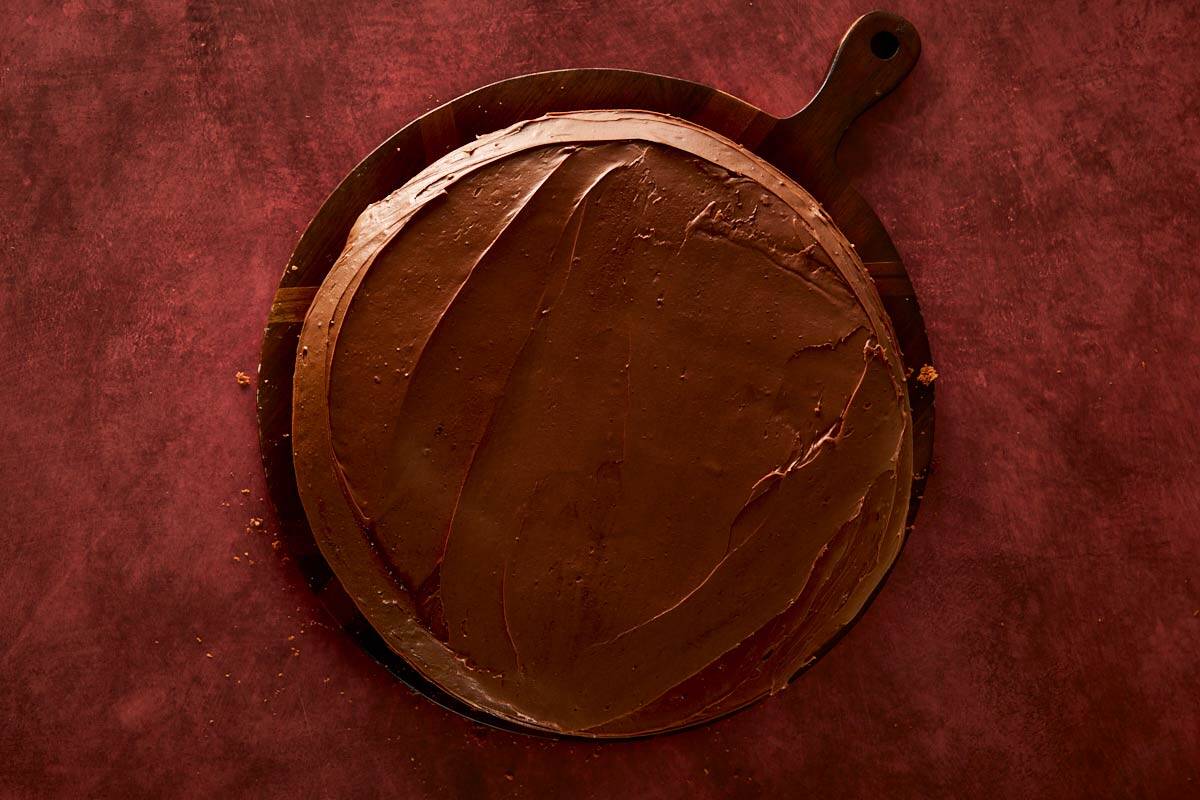 Smoothing chocolate whipped ganache over the cake layers for a glossy finish.