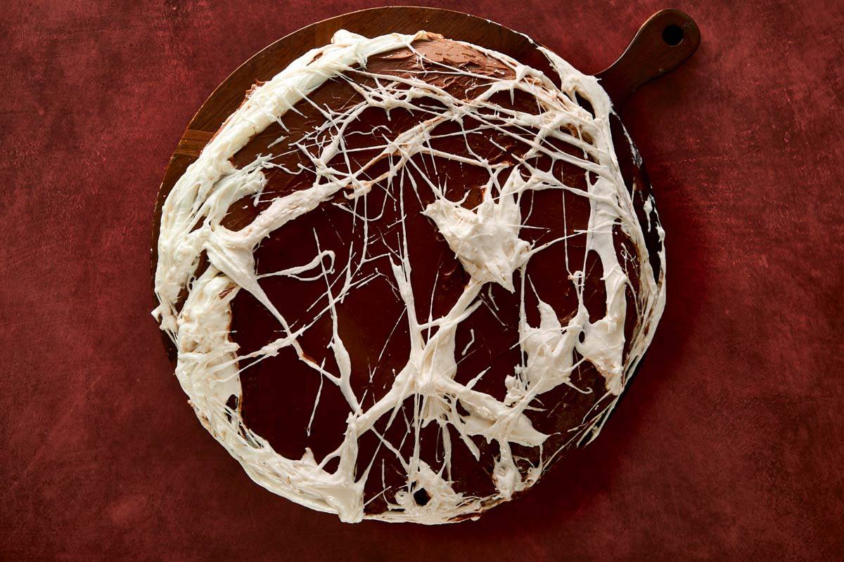 Stretching melted marshmallows over the frosted cake to form spooky web strands.