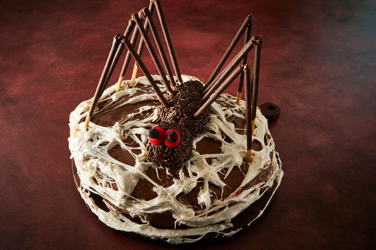Assembling the spider on top of the cake — chocolate legs, red fondant eyes, and a marshmallow web.
