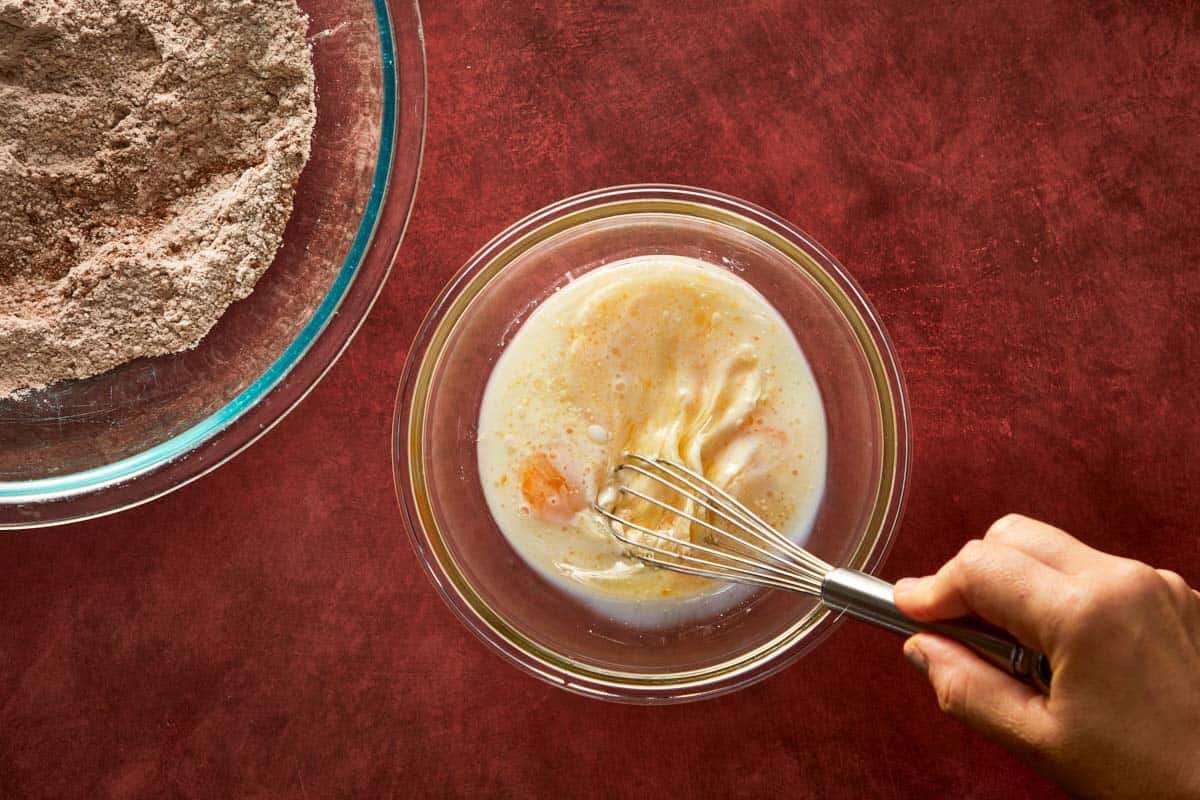 Whisking eggs, milk, and oil in a bowl to create the wet mixture for the cake batter.