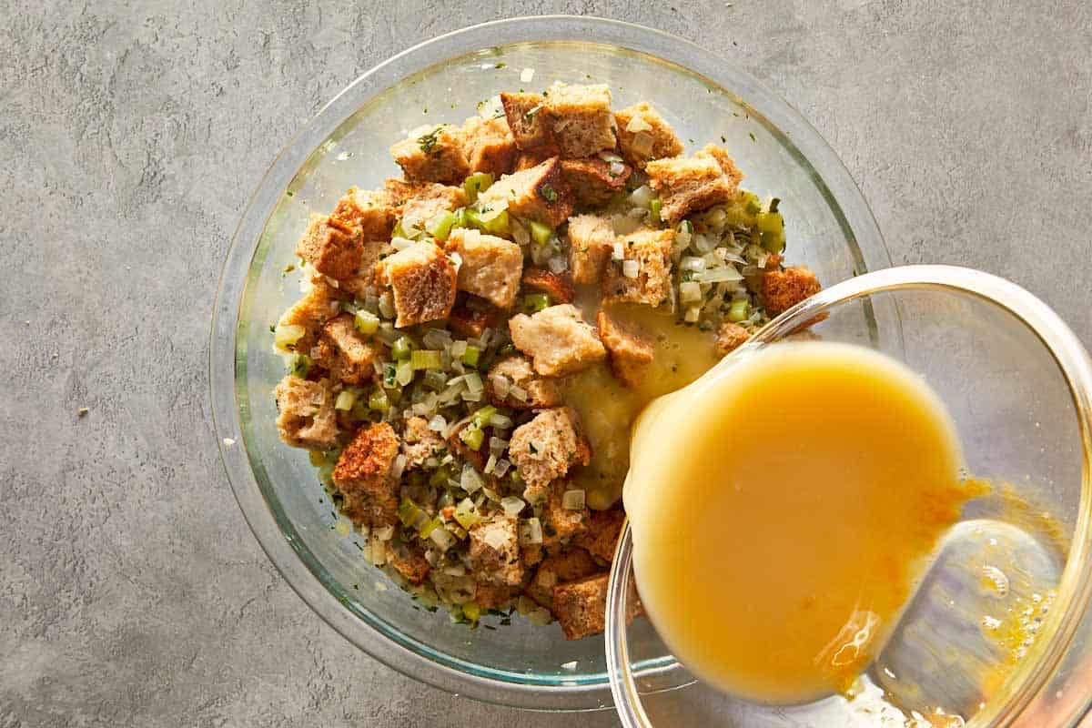 Pouring beaten eggs into the bowl of bread and vegetable mixture to bind the classic herb stuffing ingredients.