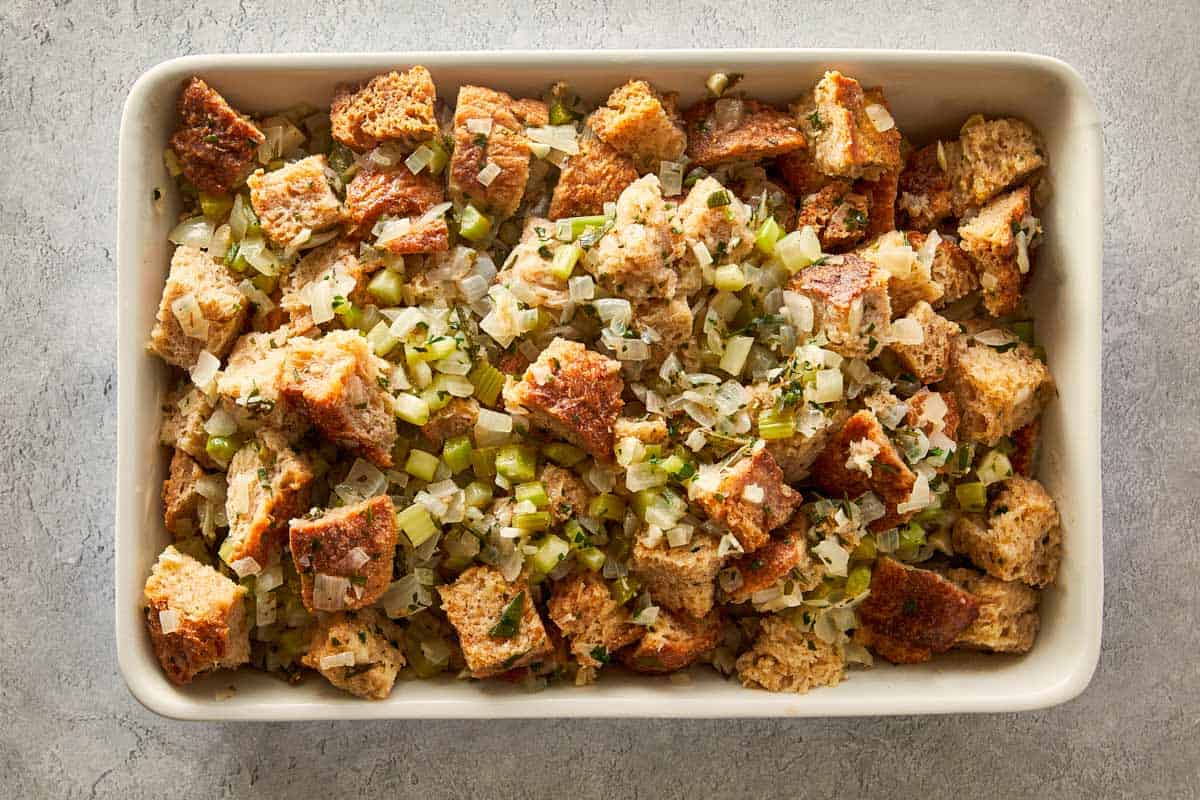 Unbaked stuffing mixture transferred and spread evenly in a white rectangular baking dish before cooking.