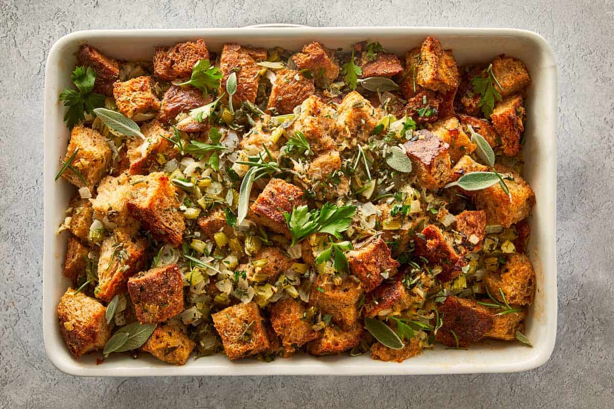 Baked buttery herb stuffing in a white casserole dish, garnished with fresh sage and parsley, a perfect holiday side dish.