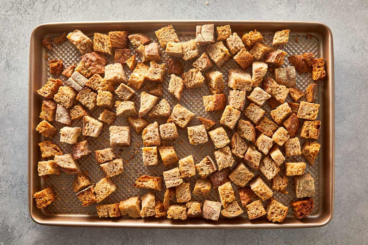 Toasted bread cubes spread out on a baking sheet, ready to be used as the base for herb stuffing.
