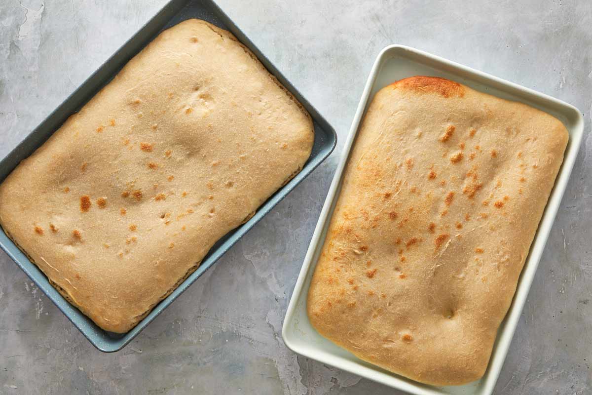 Two trays of precooked focaccia bases with golden edges just out of the oven.